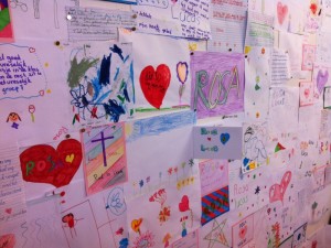 Bulletin board covered with children's drawings with Dutch text, memorializing Lucas and Rosa.