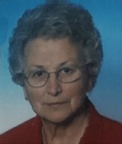 Portrait photo of Luciana Torcelli; she is an elderly woman with curly gray hair and fair skin. She is wearing a red blouse and glasses.
