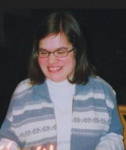 Photo of Melissa Couture, a young woman with fair skin and brown hair. She is wearing glasses and a striped sweater. She is smiling broadly and looking down at some candles.