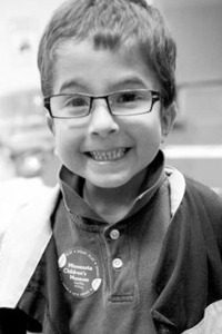 Black and white photo of Seth Johnson, a small boy wearing glasses and a polo shirt and jacket.