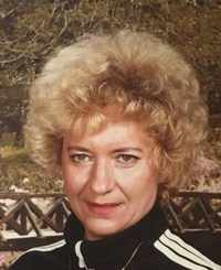 Photo of Charlene Norris. She is a middle-aged woman with short permed blond hair and fair skin, wearing a black and white track suit.