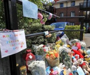 Memorial left outside Omran Omar's apartment, consisting of flowers, stuffed animals, and notes. In the foreground is a sign that says, "Rest in peace, precious little boy."