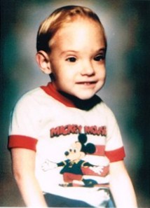 Photo of Stephen Hughes, a small boy with a large head, wearing a Mickey Mouse T-shirt; he has straight brown hair and fair skin.