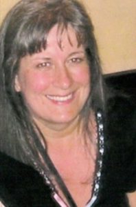 Photo of Sharon Birchwood, a woman with fair skin and straight, shoulder-length gray hair; she is wearing a black dress and smiling for the camera.
