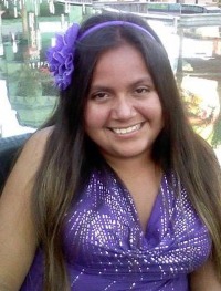 Photo of Bridget Charlebois, a young woman with tan skin and long, straight medium-brown hair. She is wearing a purple sequined tank top and a purple flower in her hair.