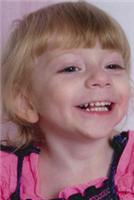 Photo of Kylee Forrest. She is a toddler with blonde hair and fair skin. She is smiling broadly. Her shirt is pink and ruffled.