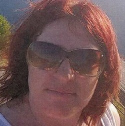 Photo of Samantha Kelly. She has fair skin and bright red shoulder-length hair, and is wearing sunglasses.