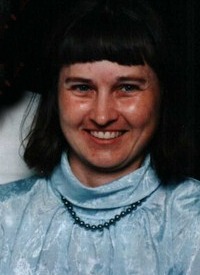 Photo of Lorraine Smith. She is a woman with light skin and straight brown hair cut to chin-length with bangs. She is smiling at the camera. She is wearing a blue silk turtleneck blouse and some blue beads.