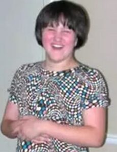 Photo of a young woman with fair skin and short brown hair, laughing; she is wearing a black and white blouse.