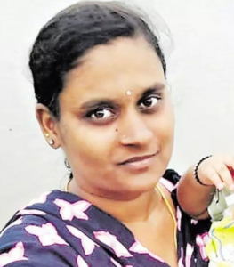 Photo of a woman with light brown skin and straight black hair pulled back in a ponytail. She has dark-brown eyes, and is wearing pearl earrings, a silver bindi, and a flowered purple top. Just to the side of the photo is the arm of a toddler that she is holding.