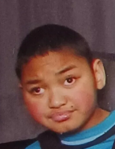 Photo of a young man with tan skin and short black hair, wearing a blue and teal sweater. 