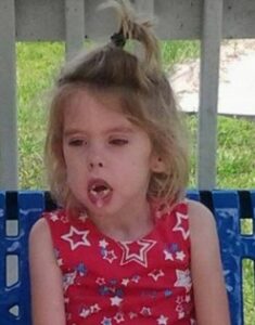 Photo of a small girl with blond hair pulled up in a ponytail on top of her head; she is wearing a pink star print shirt.