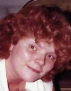 Photo of a woman with very curly auburn hair and pale skin. She is wearing a white top.