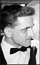Black and white photo of a young man in a tuxedo, photographed in profile; he has dark hair and a neatly trimmed mustache.