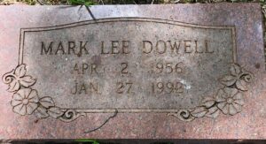 Gravestone for Mark Lee Dowell, April 2 1956 to January 27 1992. The stone is a granite plaque engraved with flowers.