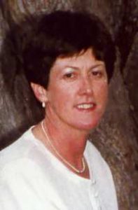 Photo of Jillian Thomas. She is a woman with ruddy skin and short brown curly hair, wearing a white blouse and earrings.