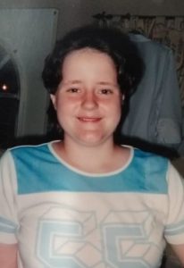 Photo of a teenage girl with short, curly brown hair and fair skin, wearing a teal-and-white sports jersey.