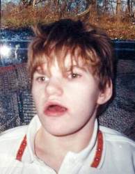 Photo of Casey Axsom, a young adult with short, messy strawberry-blonde hair, wearing a white polo shirt. Casey's mouth is slightly open.