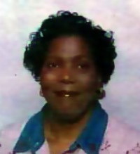 Portrait photo of a woman with dark-brown skin and curly black hair, wearing a pink blouse and turquoise scarf.