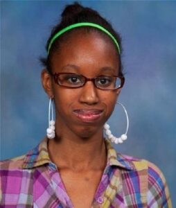 Photo of Alicia Moore, an African-American teenage girl. She is wearing a neon-green headband, big hoop earrings, and glasses.