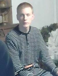 Photo of a teenage boy with light skin and a buzz cut. He is wearing a striped shirt and has a solemn expression.