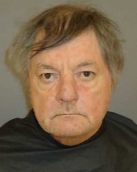 Photo of an older man with gray hair and light skin; he is staring into the camera, frowning.