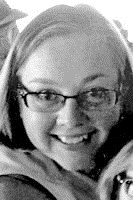 Black and white newspaper photo of a smiling girl with a round face and short, light hair. She is wearing glasses.