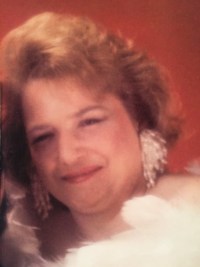 Photo of Rosemary Vincent. She is a middle-aged woman with a round face, pale skin, and short curly red hair. She is wearing big white feathered earrings.