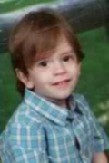 Photo of a small boy with pale skin and auburn hair, wearing a blue and white checked polo shirt.