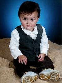 Portrait photo of a seated toddler boy with dark straight hair and fair skin, wearing a dark vest over a white dress shirt.