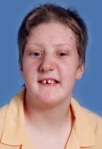 Photo: A teenage girl, her brown hair cut short. She has fair skin and blue eyes. There is a gap between her two front teeth. She is wearing a yellow polo shirt.