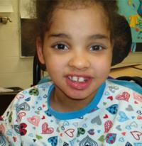 Photo of Lakesha Victor, a girl with a gap-toothed smile. Her head leans against a headrest.
