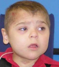 hoto of Jori Lirette, a young boy with fair skin and short blond hair in a buzz cut, wearing an orange striped polo shirt.