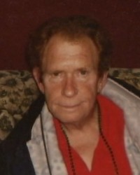 Photo: An older man, balding, with brown hair, wearing a jacket and red shirt. 