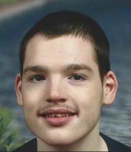 Photo of a young man with fair skin, short brown hair, and a think mustache; he is smiling.