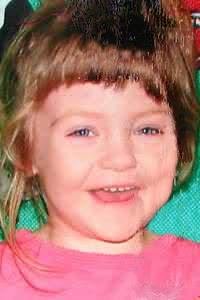 Photo of Raelynn Mascal, a girl with messy brown hair cut in bangs, fair skin, and blue eyes; she is smiling, wearing a pink sweater.