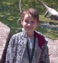 Photo of a thin teenage boy with sandy hair and pale skin, wearing a black and white print jacket and a lanyard.