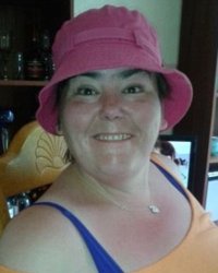 Photo of Carolyn Hyatt. She is a middle-aged woman with dark hair and fair skin, wearing a pink hat and blue-and-yellow tank top.