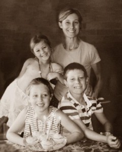 Sepia-tone portrait photo of a woman and three children, a boy and two girls. They are smiling at the camera.