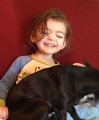 Photo of Harmony Carsey, a toddler girl. She has brown hair and fair skin, and she is holding a dog on her lap.