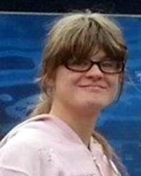 Photo of Holli Jeffcoat. She has pale skin and bushy sandy-blonde hair; she is wearing glasses and a pink sweater.