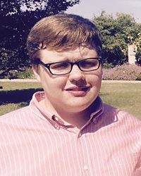 Photo of Daniel Joost, a teenage boy with fair skin and short light-brown, wavy hair. He is wearing dark-rimmed glasses and a dress shirt. Photographed outdoors, he squints into the sun.