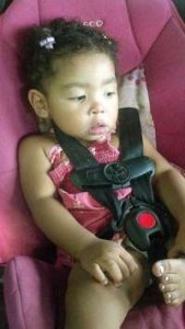 Photo of Saharah Weatherspoon, a toddler girl sitting in a pink car seat. She has very curly black hair and brown skin.