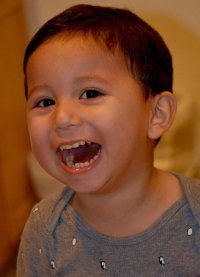 Photo of Pepe Castillo-Cisneros. He is a toddler boy with tan skin and dark brown hair, and is smiling widely with his mouth open.