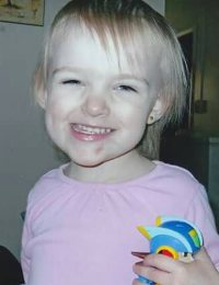 Photo of Brielle Gage, a toddler girl with very light, straight hair, wearing a pink t-shirt and holding a colorful toy. There is a small bruise on her chin.