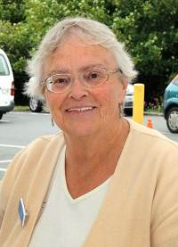 Photo of Dawn Green, an elderly white woman wearing glasses and a yellow shirt with a name tag pinned to it.