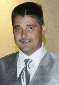 Photo of Martin Duram. He is a light-skinned man with dark hair and mustache, wearing a silver suit and tie.
