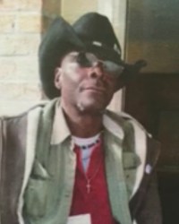 Photo of Cedric Page, an African-American man wearing a cowboy hat, brown jacket, sunglasses, and a small gold cross necklace.