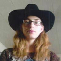 Photo of Joyce Taylor. She is a young woman with long blond hair and glasses, wearing a wide-brimmed black hat.