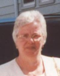 Photo of Maria Branco. She is an elderly woman with short white hair, and fair skin. She is wearing glasses and a white blouse, squinting slightly into the sun.
